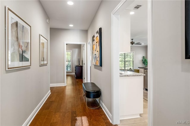 hall with plenty of natural light, wood finished floors, visible vents, and baseboards