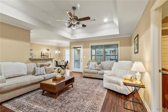 living room featuring a raised ceiling, ornamental molding, dark hardwood / wood-style floors, and ceiling fan