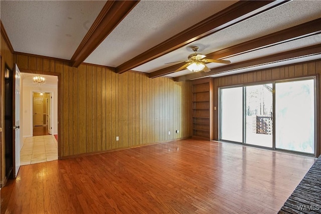 unfurnished room with a textured ceiling, light hardwood / wood-style floors, beamed ceiling, and wood walls