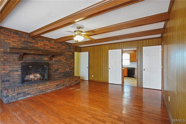 unfurnished living room with wood-type flooring, a fireplace, wooden walls, and beamed ceiling