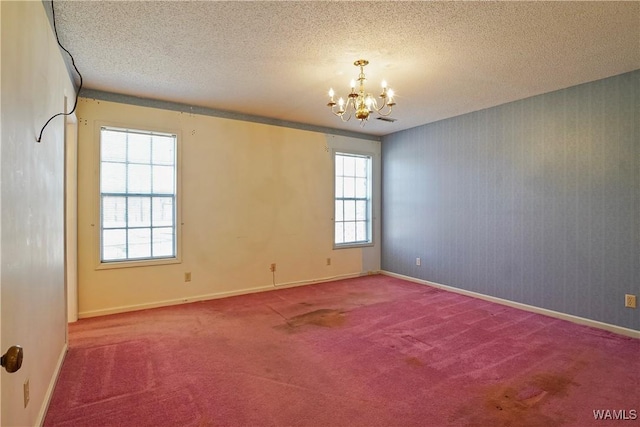 carpeted spare room with a notable chandelier, a wealth of natural light, and a textured ceiling