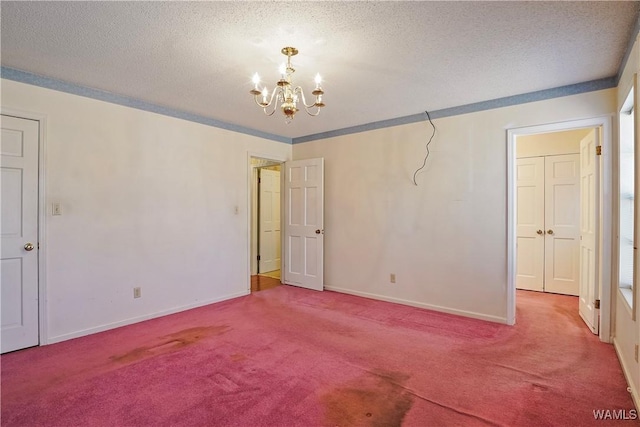 spare room with an inviting chandelier, carpet floors, ornamental molding, and a textured ceiling