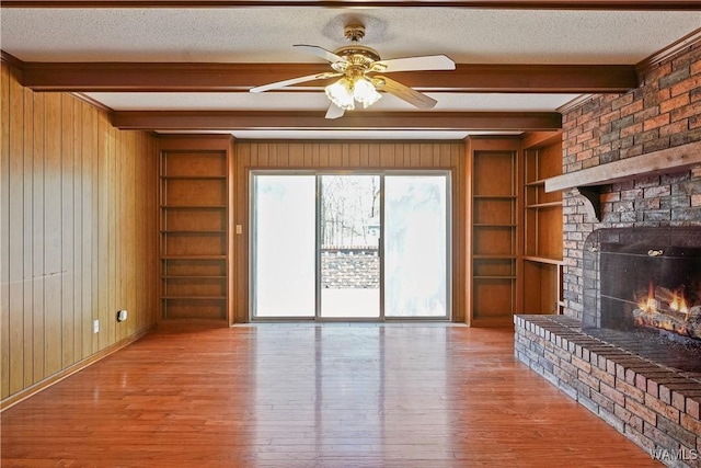 unfurnished living room featuring a brick fireplace, light hardwood / wood-style flooring, beam ceiling, and built in shelves