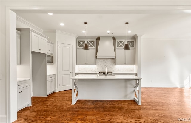 kitchen featuring custom range hood, dark hardwood / wood-style floors, a center island with sink, and pendant lighting