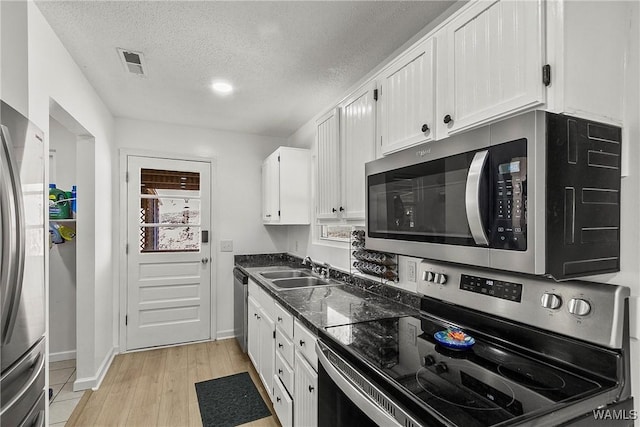 kitchen with a textured ceiling, stainless steel appliances, a sink, visible vents, and white cabinetry