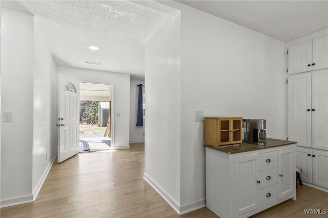 hallway with a textured ceiling, light wood finished floors, and baseboards