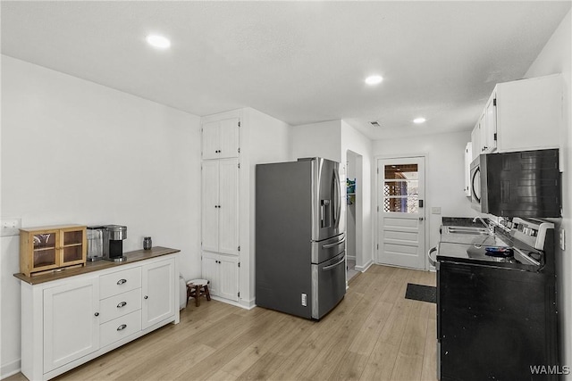 kitchen with appliances with stainless steel finishes, white cabinetry, and light wood-style flooring