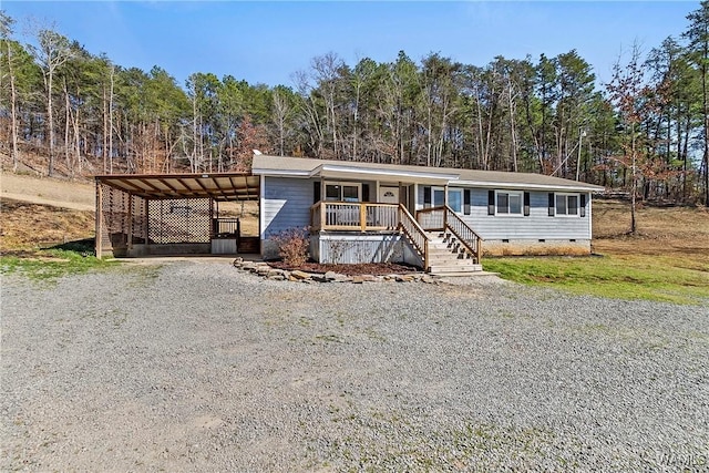 manufactured / mobile home featuring crawl space, covered porch, driveway, and a wooded view