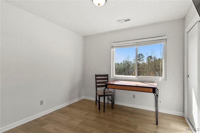 office space with baseboards, a textured ceiling, visible vents, and wood finished floors