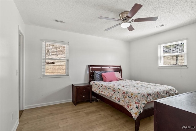 bedroom featuring light wood-type flooring, ceiling fan, visible vents, and a textured ceiling