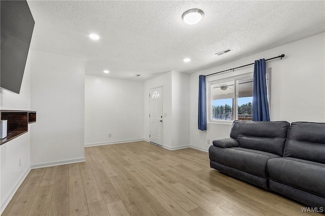 living room featuring a textured ceiling, light wood finished floors, visible vents, and baseboards