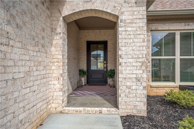 property entrance with a shingled roof and brick siding