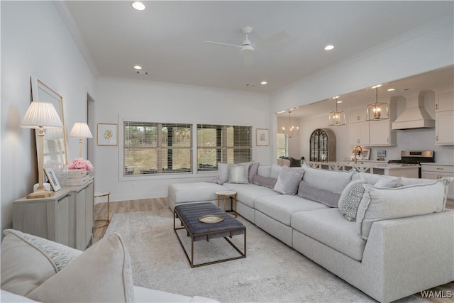 living area featuring light wood finished floors, ceiling fan with notable chandelier, ornamental molding, and recessed lighting