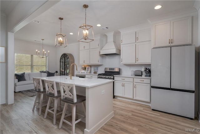 kitchen with a sink, white cabinetry, fridge, custom exhaust hood, and gas stove