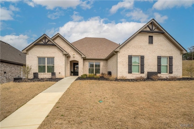 view of front of property with brick siding, a front lawn, and roof with shingles