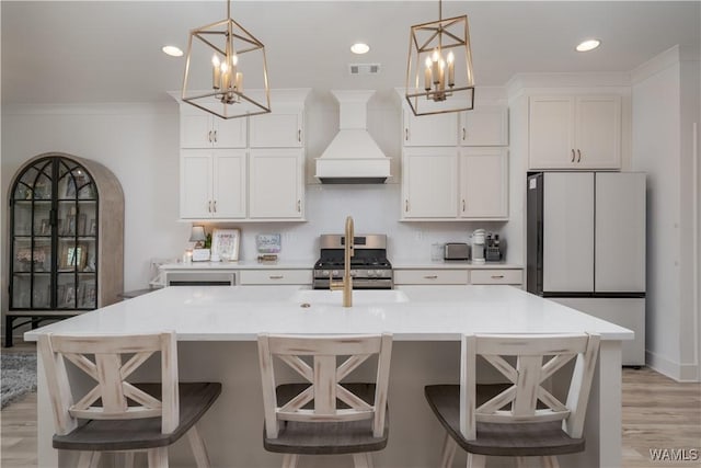 kitchen featuring stainless steel gas range oven, a kitchen island with sink, visible vents, freestanding refrigerator, and custom range hood