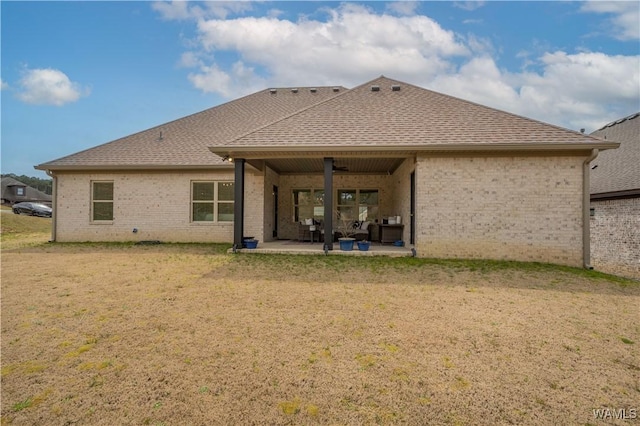 rear view of house featuring a patio area, a yard, brick siding, and roof with shingles