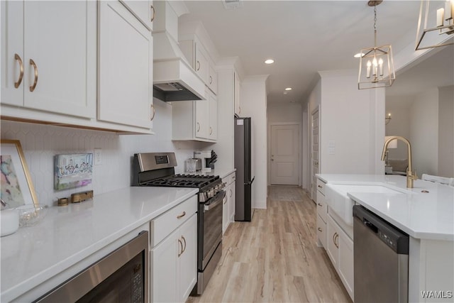 kitchen with white cabinets, appliances with stainless steel finishes, custom exhaust hood, light countertops, and a sink