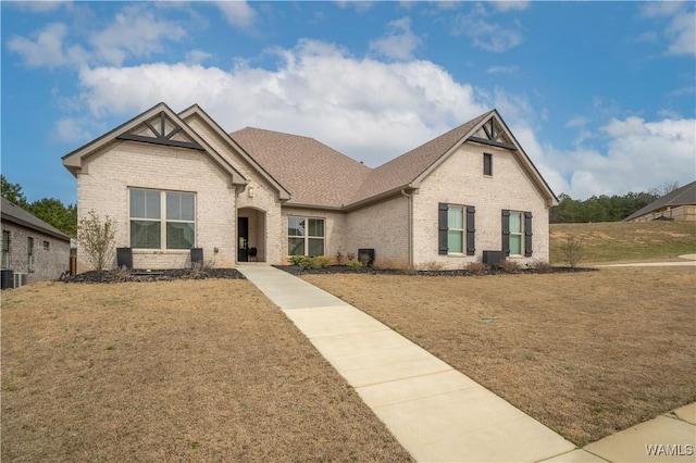 view of front facade featuring a shingled roof, a front yard, and brick siding