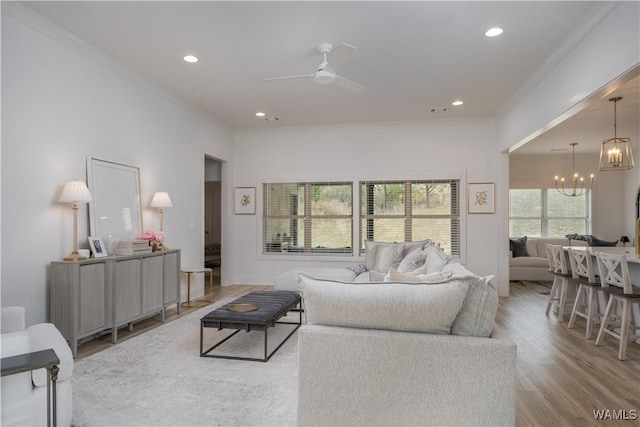 living room with recessed lighting, ornamental molding, wood finished floors, and ceiling fan with notable chandelier