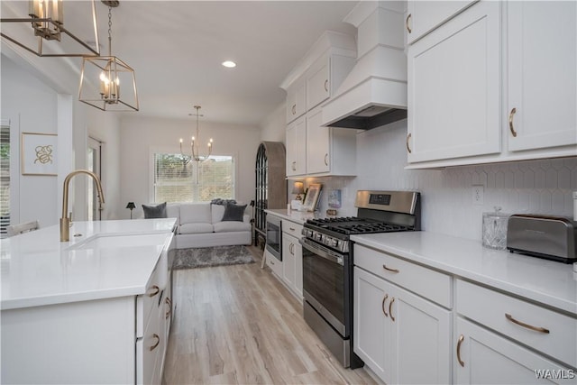 kitchen with decorative backsplash, custom range hood, an inviting chandelier, stainless steel appliances, and a sink