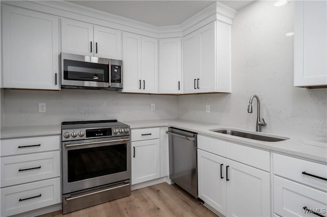 kitchen with light wood-type flooring, light countertops, appliances with stainless steel finishes, white cabinets, and a sink