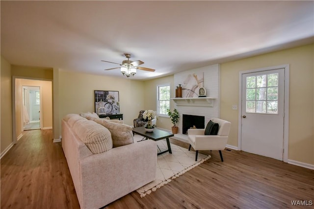 living area with a ceiling fan, a fireplace, baseboards, and wood finished floors