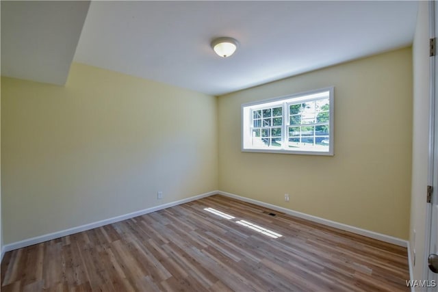 empty room featuring baseboards, visible vents, and wood finished floors