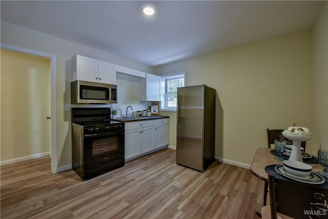 kitchen featuring baseboards, white cabinets, stainless steel appliances, light wood-style floors, and a sink