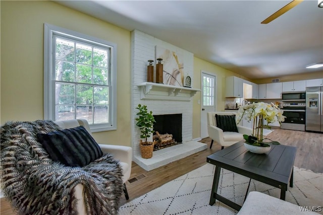 living room with light wood-style floors, visible vents, and a fireplace