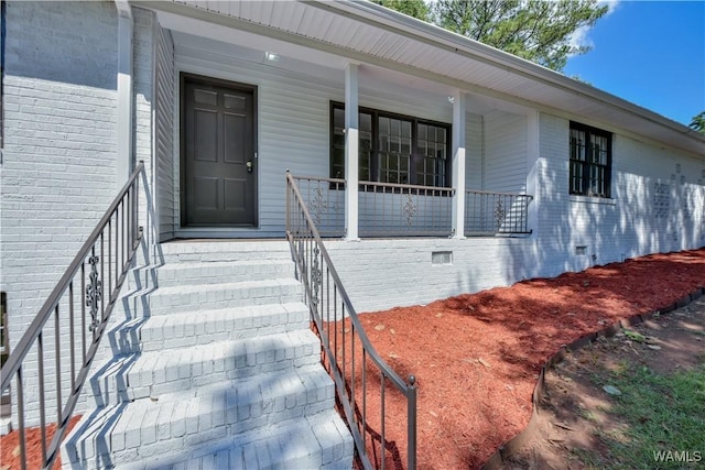 entrance to property featuring covered porch, brick siding, and crawl space