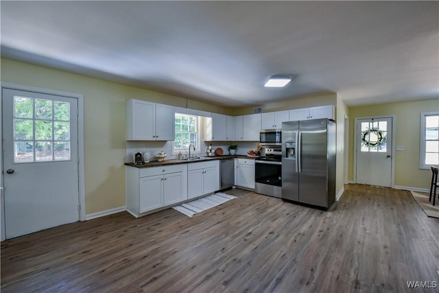 kitchen with dark wood-style floors, dark countertops, appliances with stainless steel finishes, white cabinetry, and a sink