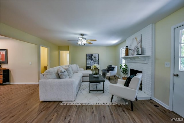 living area featuring a brick fireplace, ceiling fan, baseboards, and wood finished floors