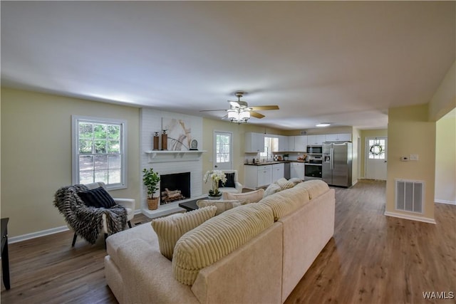 living area featuring a wealth of natural light, a brick fireplace, visible vents, and wood finished floors