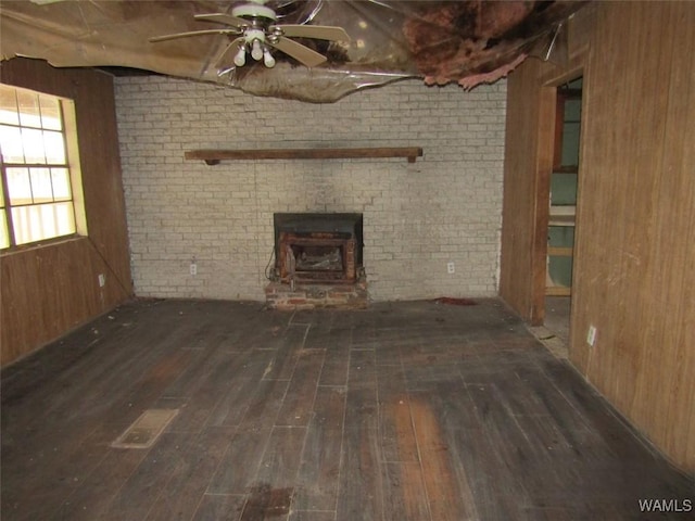 unfurnished living room featuring wood walls, ceiling fan, brick wall, and dark wood-type flooring