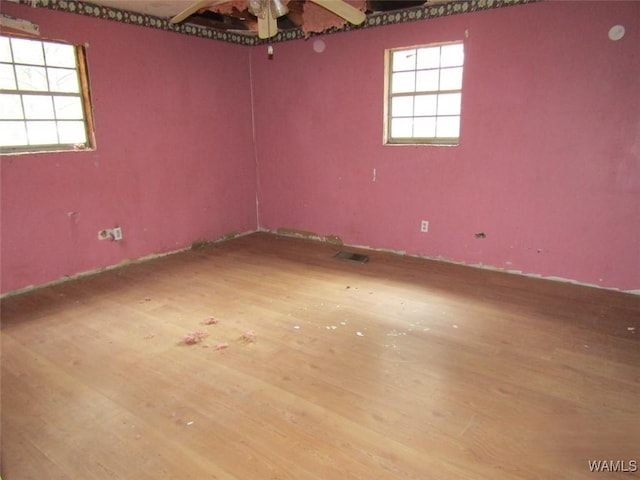 unfurnished room featuring wood finished floors, visible vents, and a healthy amount of sunlight