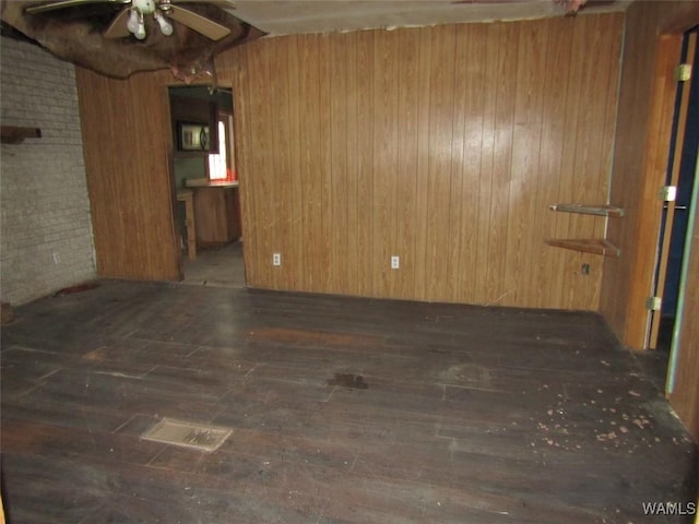 spare room featuring dark wood-style floors, brick wall, wooden walls, and a ceiling fan