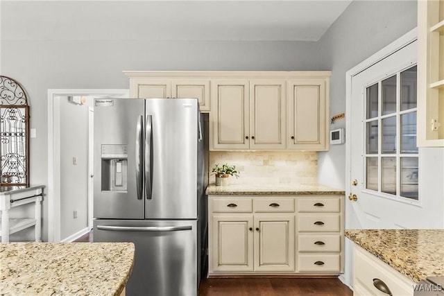 kitchen featuring dark wood-type flooring, light stone counters, backsplash, stainless steel fridge, and cream cabinets