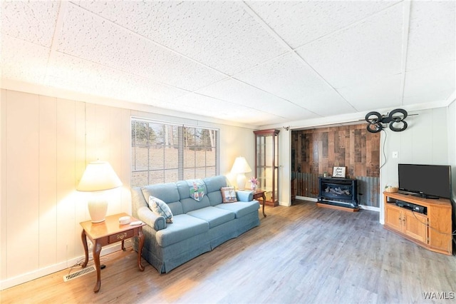 living room with light wood finished floors, a paneled ceiling, a wood stove, and baseboards