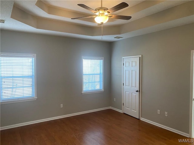 unfurnished room with baseboards, visible vents, a ceiling fan, dark wood-type flooring, and a tray ceiling