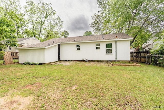 back of property with fence, roof with shingles, and a lawn