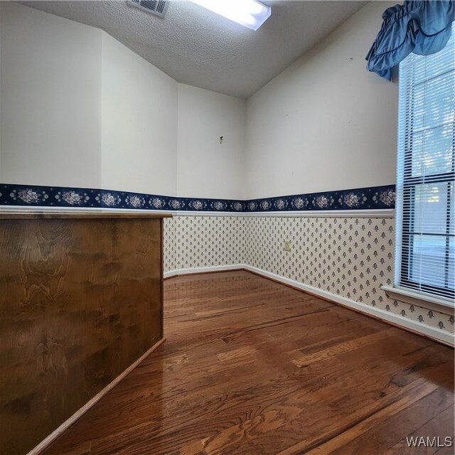 empty room with wood-type flooring, a textured ceiling, and vaulted ceiling