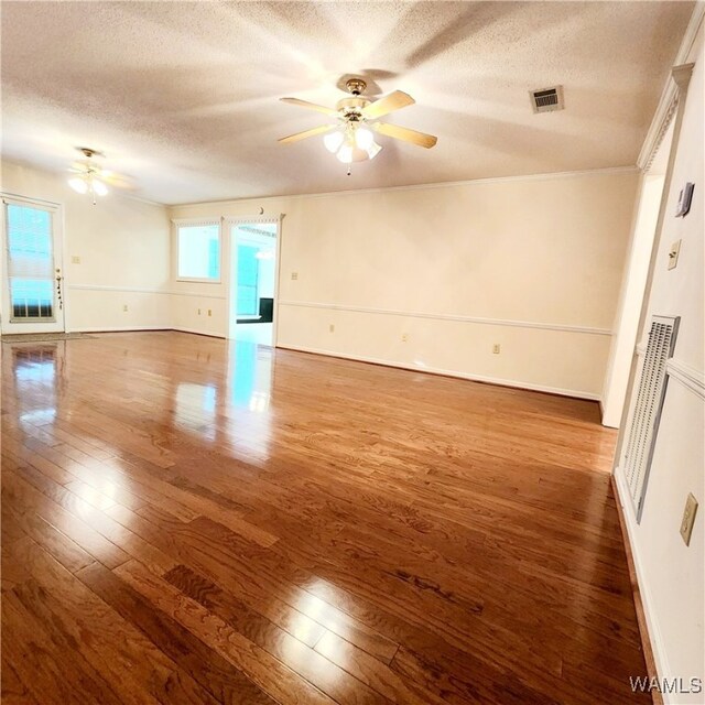 empty room with a textured ceiling, ceiling fan, crown molding, and dark wood-type flooring