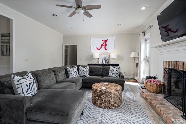 living room featuring hardwood / wood-style flooring, ceiling fan, crown molding, and a brick fireplace