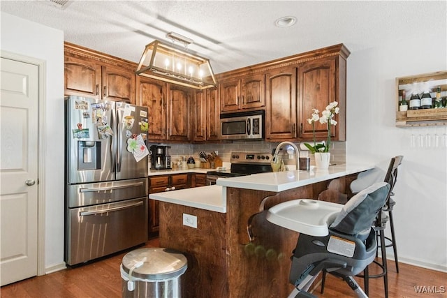 kitchen featuring a peninsula, a kitchen breakfast bar, dark wood-style floors, tasteful backsplash, and stainless steel appliances