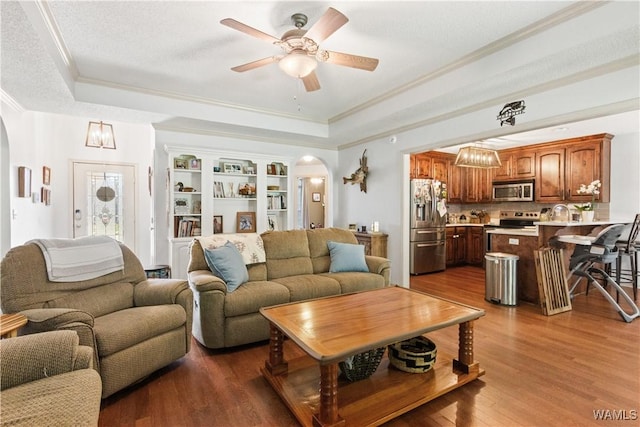 living room featuring crown molding, arched walkways, and a tray ceiling