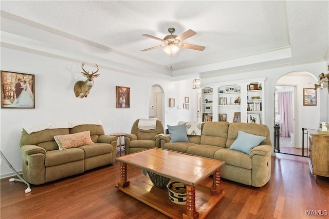 living room featuring arched walkways, a ceiling fan, dark wood-style floors, and a raised ceiling