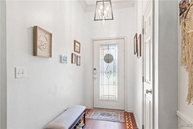 doorway featuring baseboards, ornamental molding, wood finished floors, and a notable chandelier