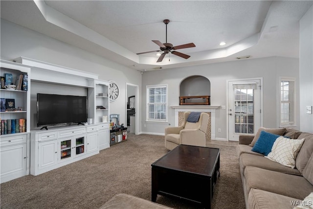 carpeted living room with a raised ceiling, a high end fireplace, and ceiling fan