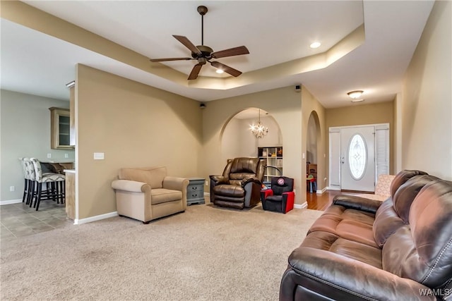 living room with a tray ceiling, ceiling fan with notable chandelier, and light colored carpet